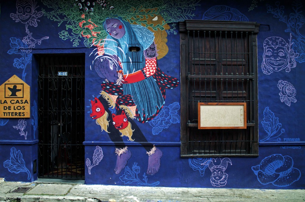 Fachada de la Casa de los Títeres en el barrio San Antonio, con un mural de colores y el letrero de la casa junto a la puerta.